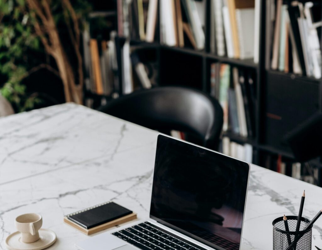 A modern minimalist workspace featuring a laptop, notebook, and coffee cup on a marble table.